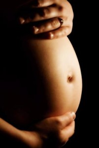 A pregnant woman holding her belly in the dark.